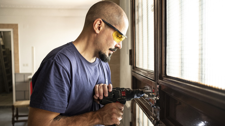 Man using power drill on door with serious expression