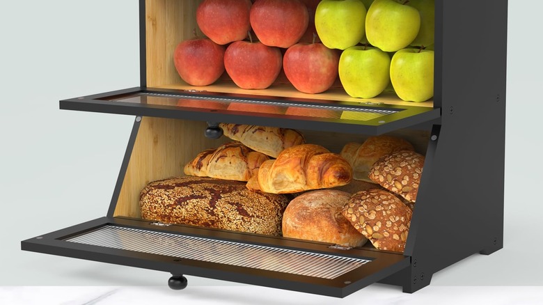 An open breadbox with bread and apples on the counter