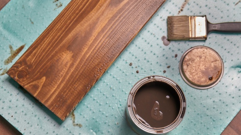 Board with fresh coat of stain on green mat next to open can of stain and brush