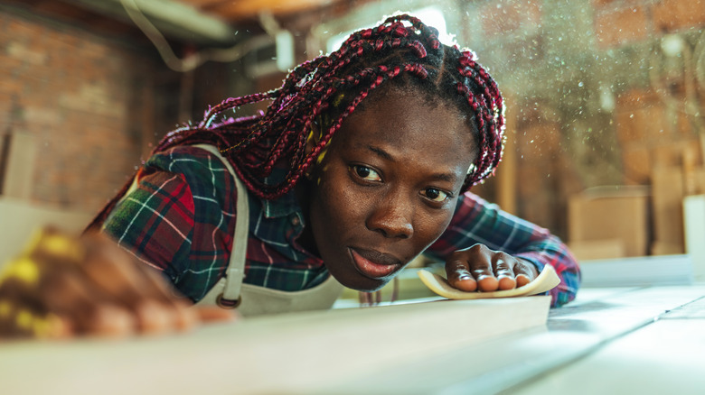 An woman smooths a board with sandpaper.