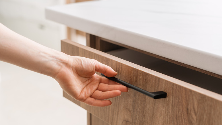 A hand opens a wooden cabinet drawer