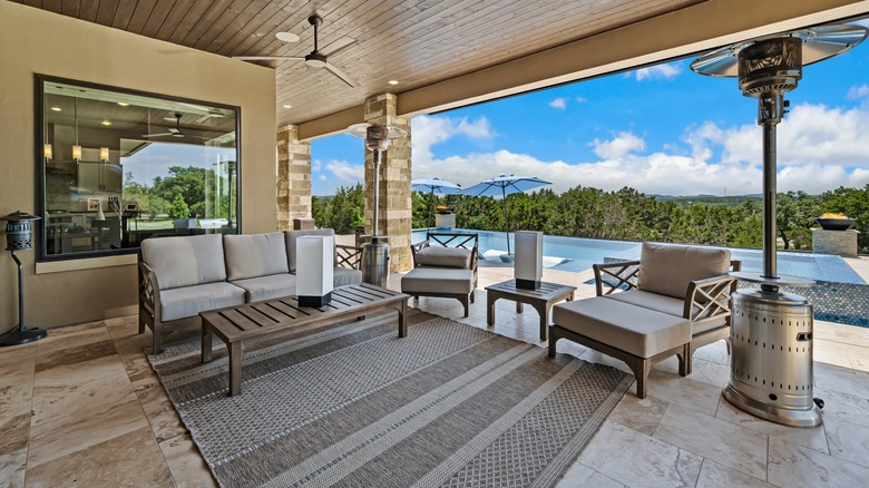 A patio with a stamped concrete floor is decorated with a ceiling fan, outdoor heater, and modern furniture