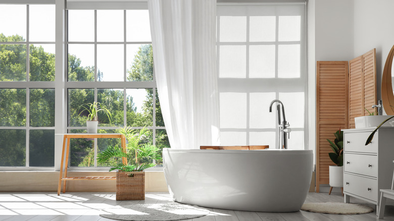 A modern bathroom with sheer curtains over a picture window