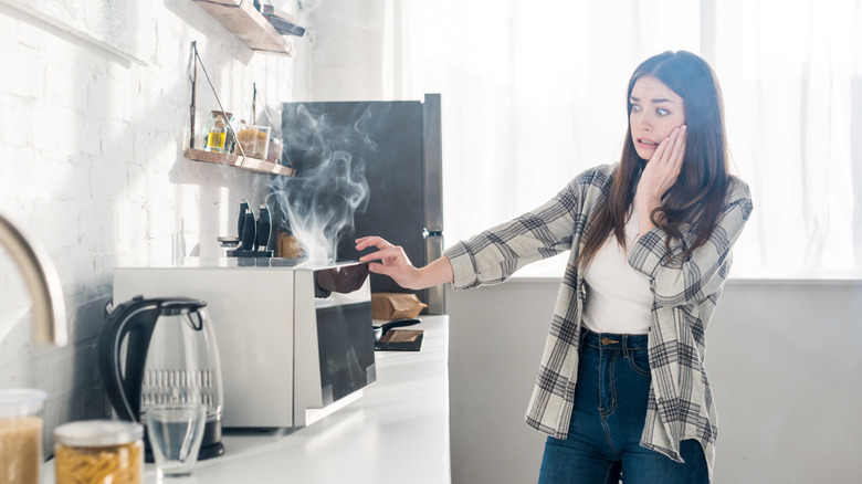 Woman looking at her broken, smoking microwave in the kitchen