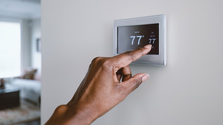 Woman setting digital thermostat on the wall.