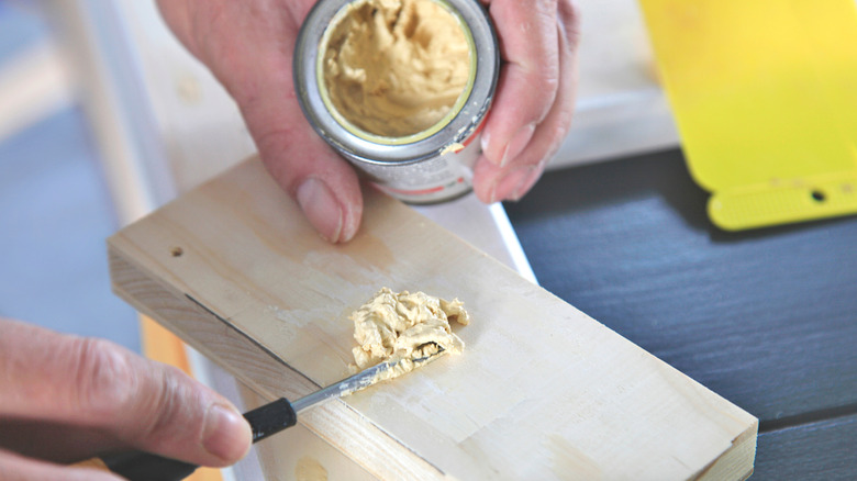 Person applying wood filler to small wooden board