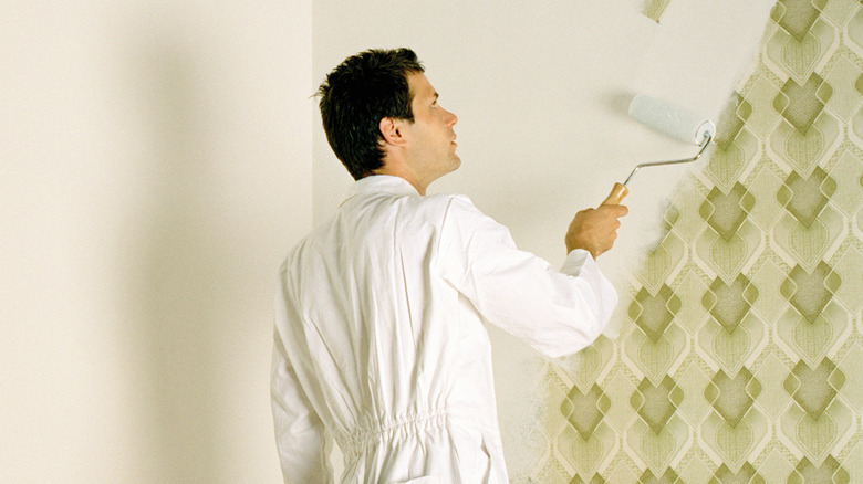 Man painting wallpapered walls