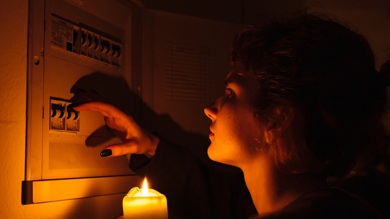 Person with a candle looking at their breaker during a power outage