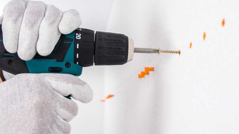 Person in work gloves drilling screw into orange wall anchor in new drywall