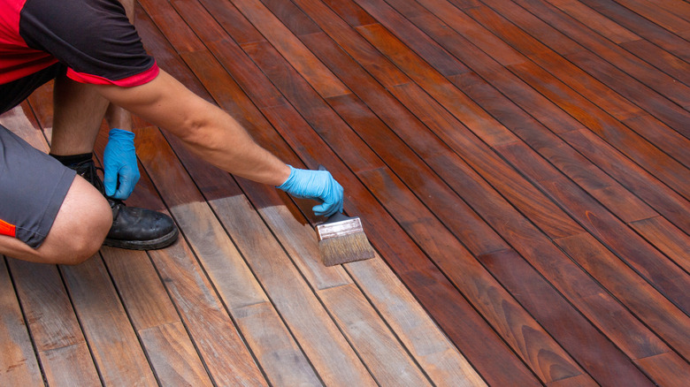 Person applying dark wood stain to deck boards