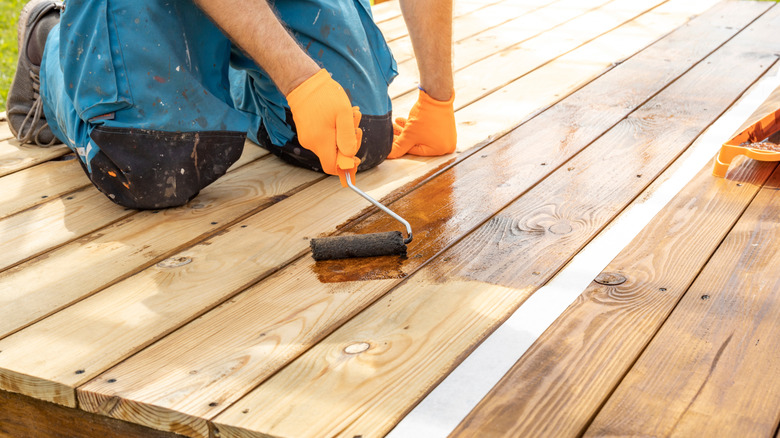 Person applying wood stain to a deck with a roller