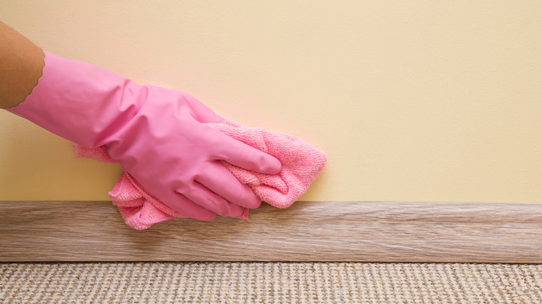 Person's hand cleaning the bottom of a wall with soft cloth.