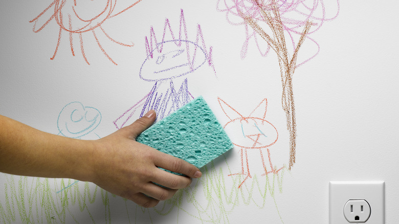 Person using a sponge to clean crayon drawing from wall.