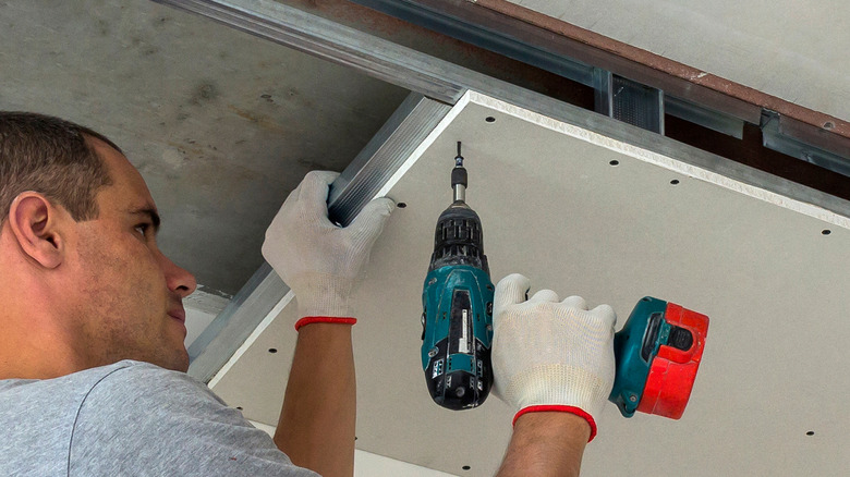 Man drilling drywall onto ceiling