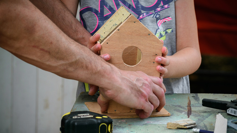 Hands building wooden birdhouse