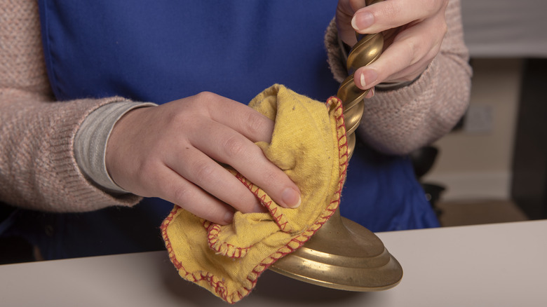 A person using a yellow cloth to clean brass candlesticks