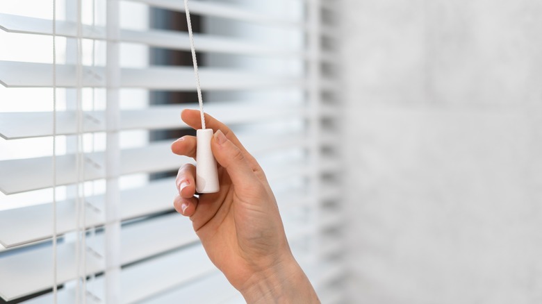 Woman pulls the adjustment string that opens window blinds