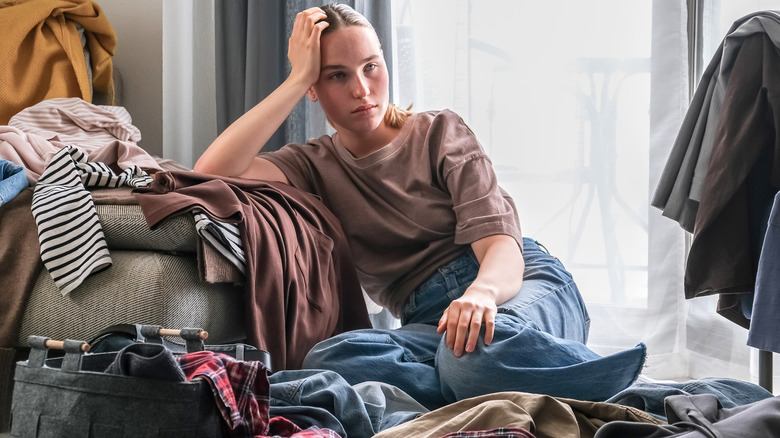 A person overwhelmed by organizing clothes tidying up a messy room