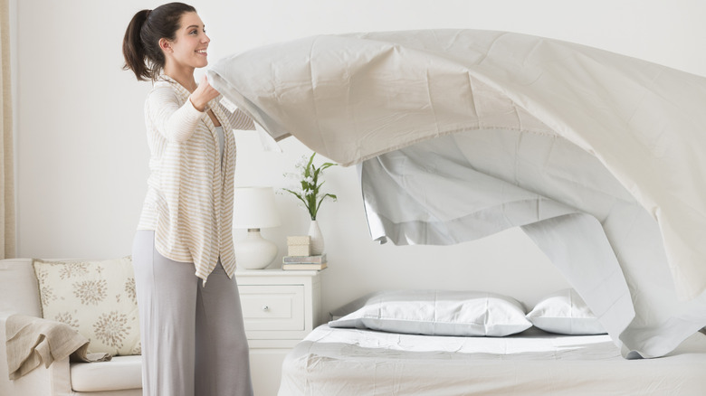 A person smiling and making a bed