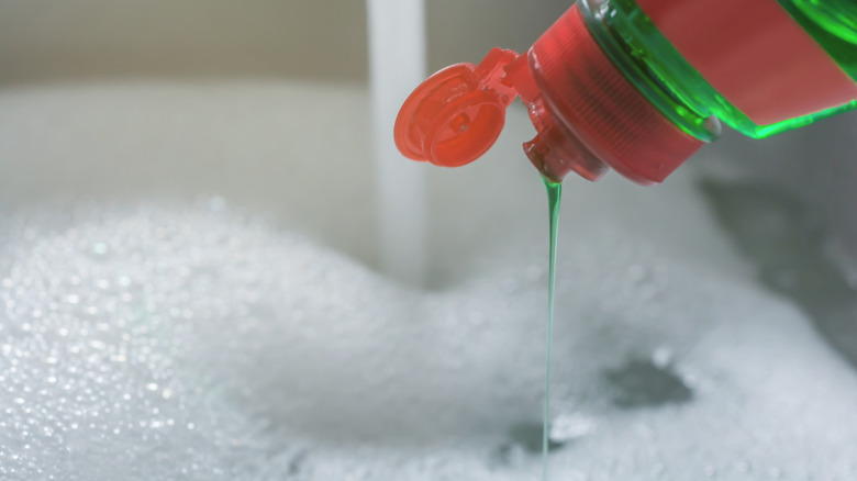 Dish soap being poured into a sink of soapy water