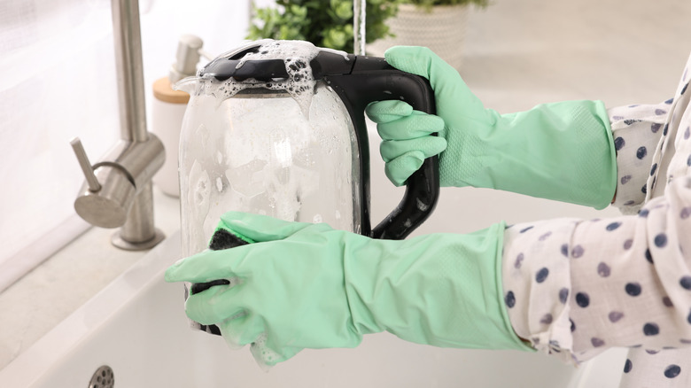 Hands washing a electric kettle with sponge at sink in kitchen