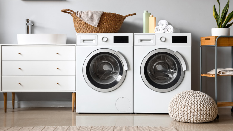 Laundry room with washer, dryer, white cabinet, and a braided ottoman