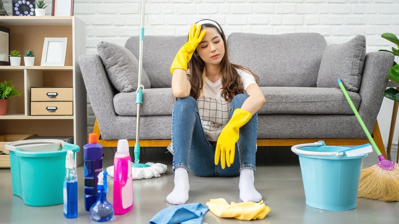 Stressed woman with cleaning supplies