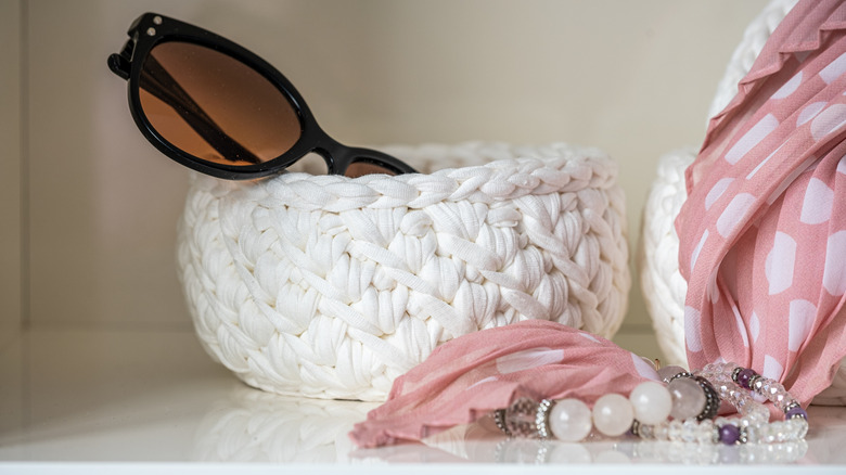 two woven white basket with sunglasses in one and a scarf in the other