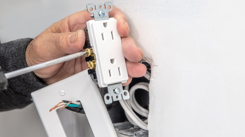 An electrician connects electrical wires to an outlet before installing it