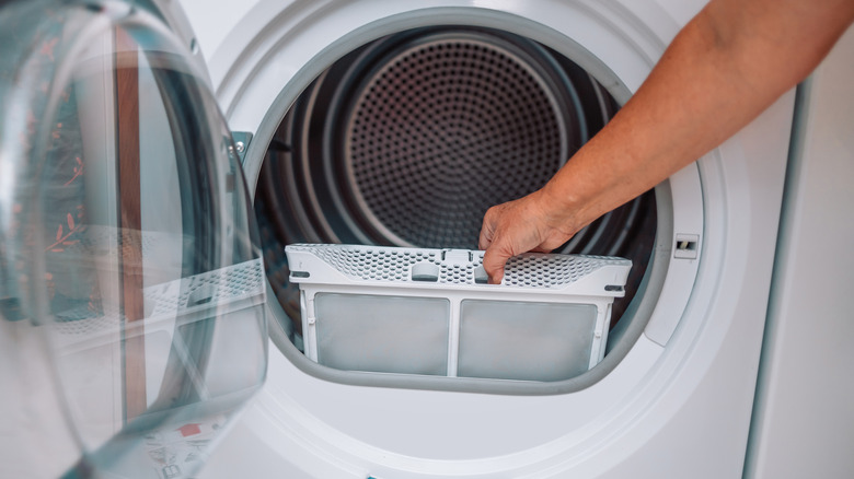 An outstretched arm is pulling out a dryer filter from inside the drum.