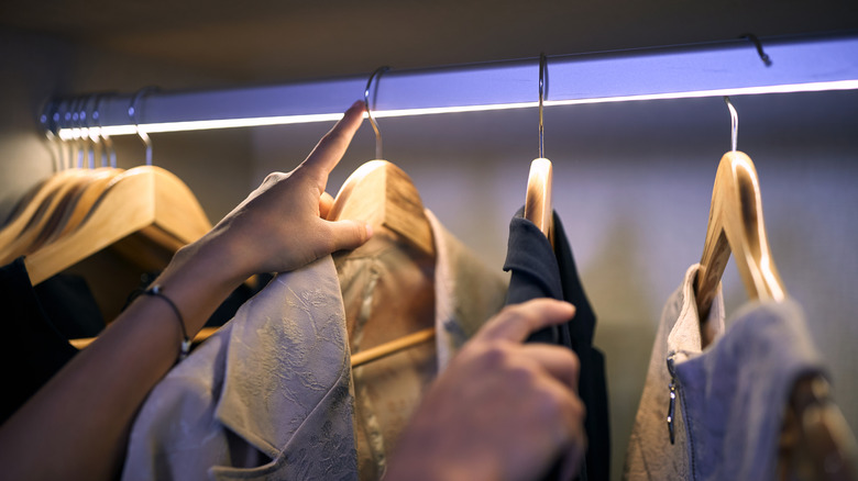 Female hand collecting clothes from closet with under rod lighting