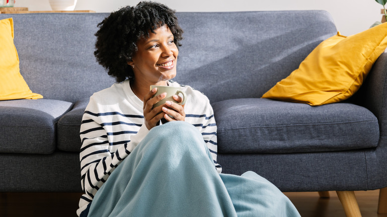 A woman holding a mug and covered with a blanket