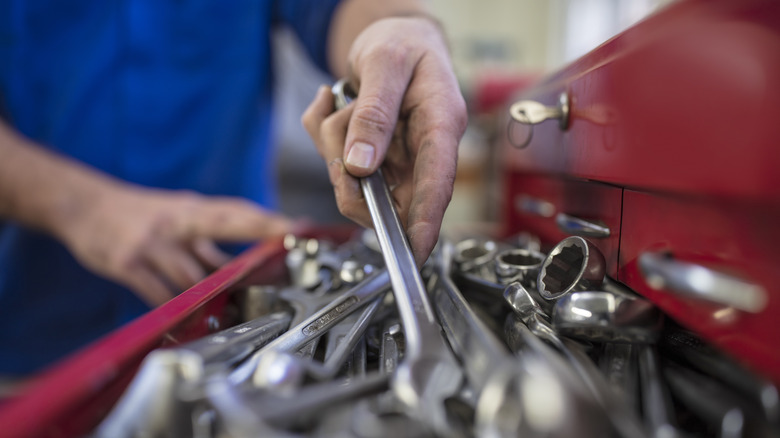 Person putting a wrench back into a disorganized toolbox