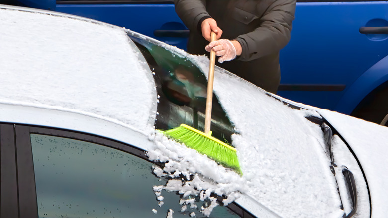 person sweeping snow off car