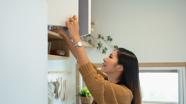 A woman reaching into her tall kitchen cabinets.