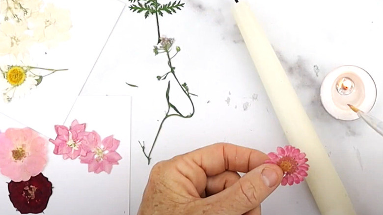 Fingers pressing flowers onto candle