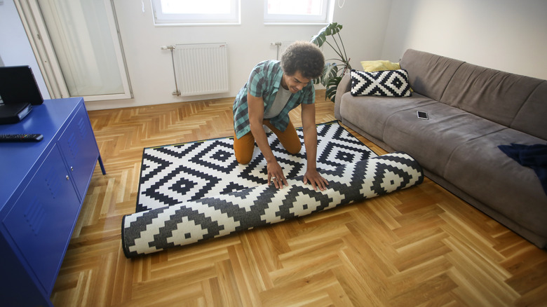 man rolling out rug on wooden floor