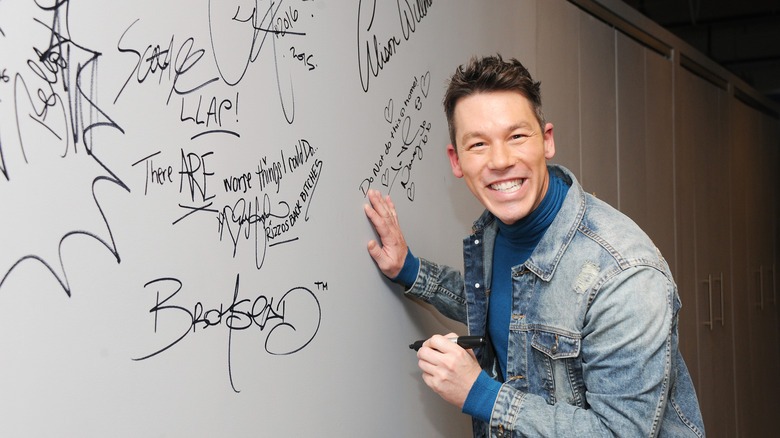 David Bromstad smiling with marker in front of a wall covered with signatures