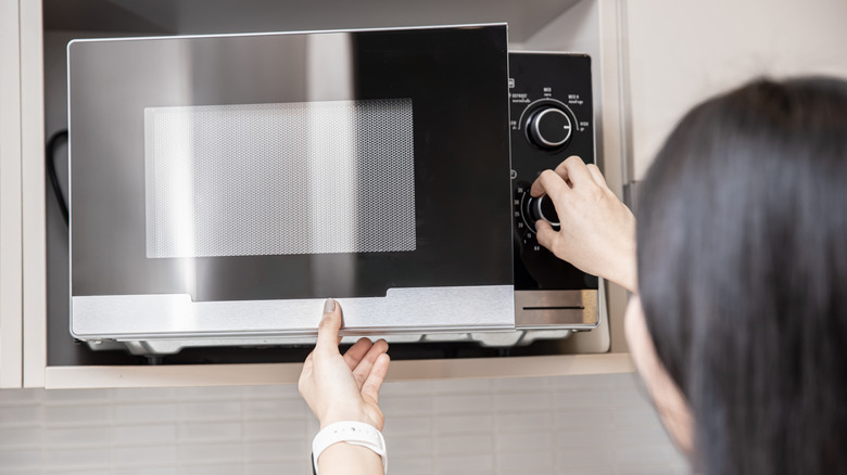 A person adjusting the time to reheat food in the microwave