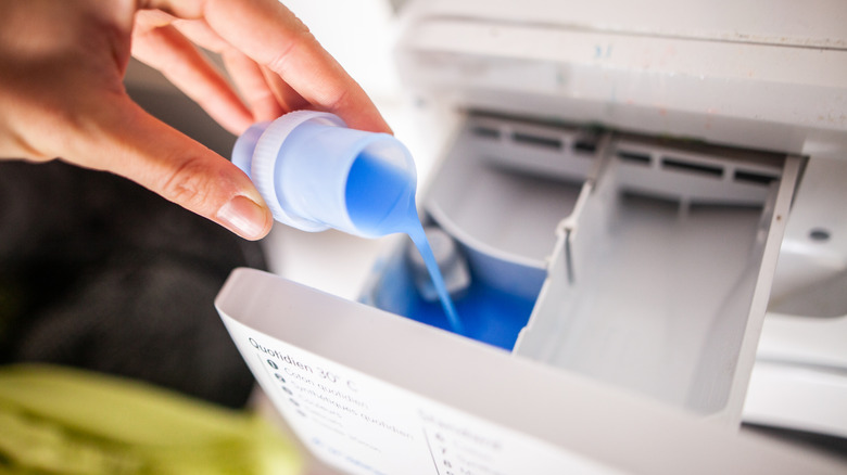 A hand pouring blue liquid laundry soap into machine