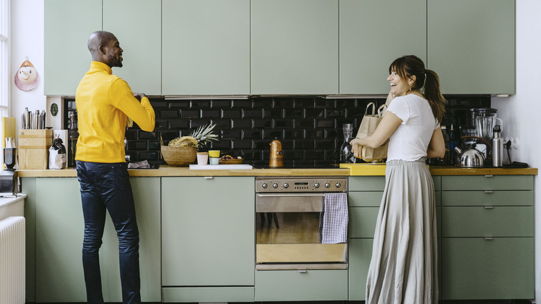 Couple unpacking groceries in a kitchen with light green cabinets