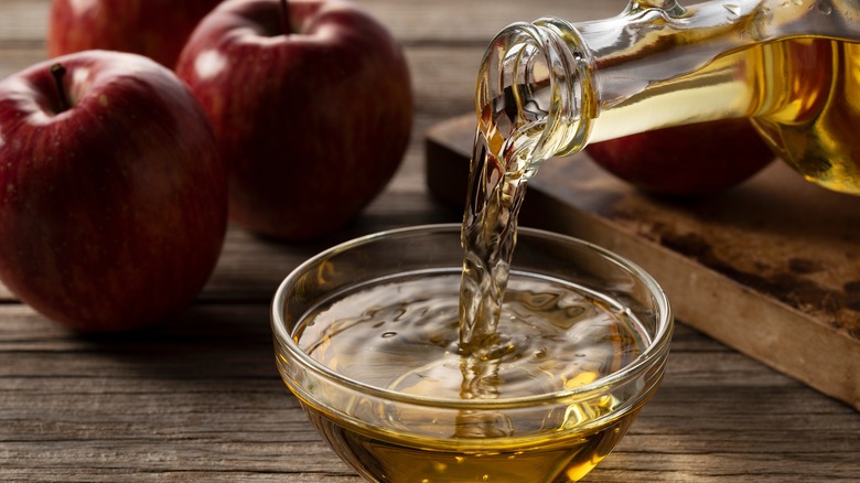 Apple cider vinegar poured in bowl with apples in background