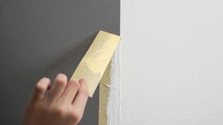 Hand peeling masking tape from a wall