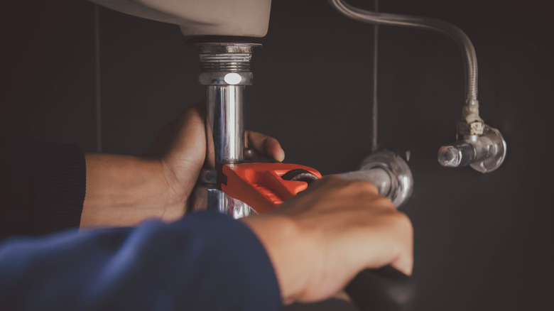 A person fixes plumbing under a sink.