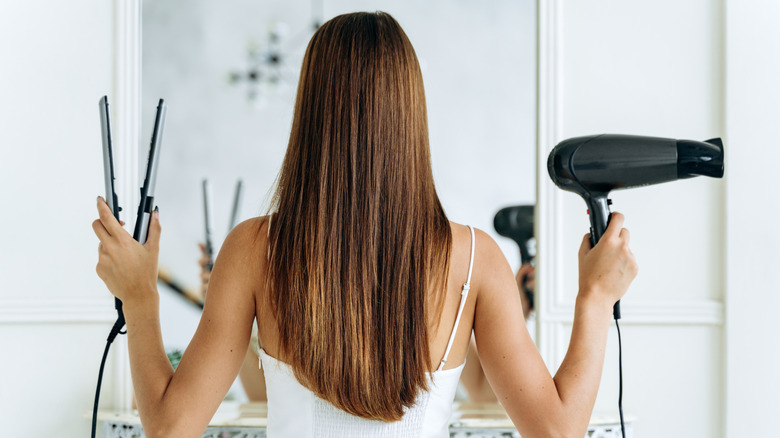 Woman holds flat iron and hair dryer
