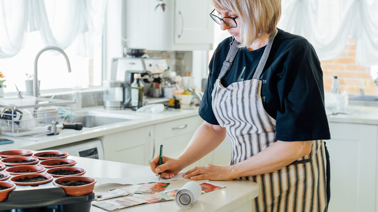 Woman in bright kitchen writing labels for seeds planted in pots