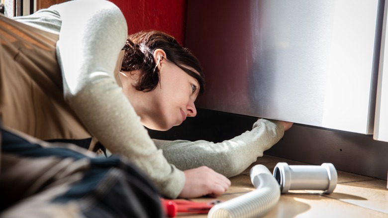 Female plumber fixing dishwasher issues with pipe and wrench on floor