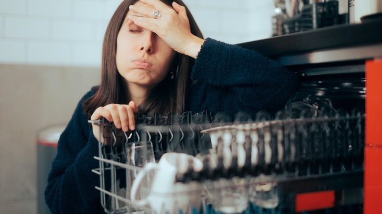 An unhappy woman sitting beside an open dishwasher