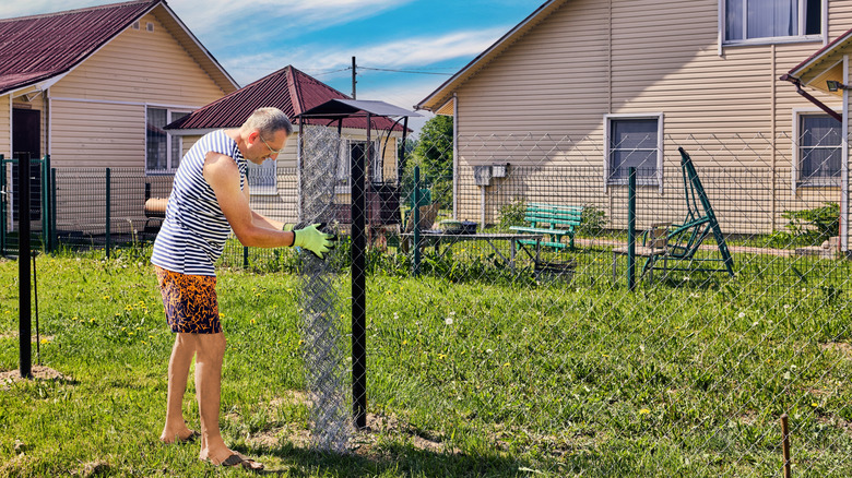 Homeowner unwinds a roll of chain link fence during installation