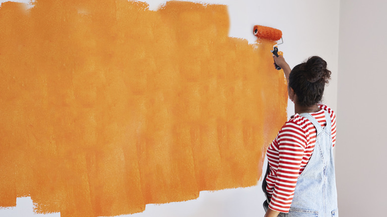 A person is painting a large swatch of the room orange.